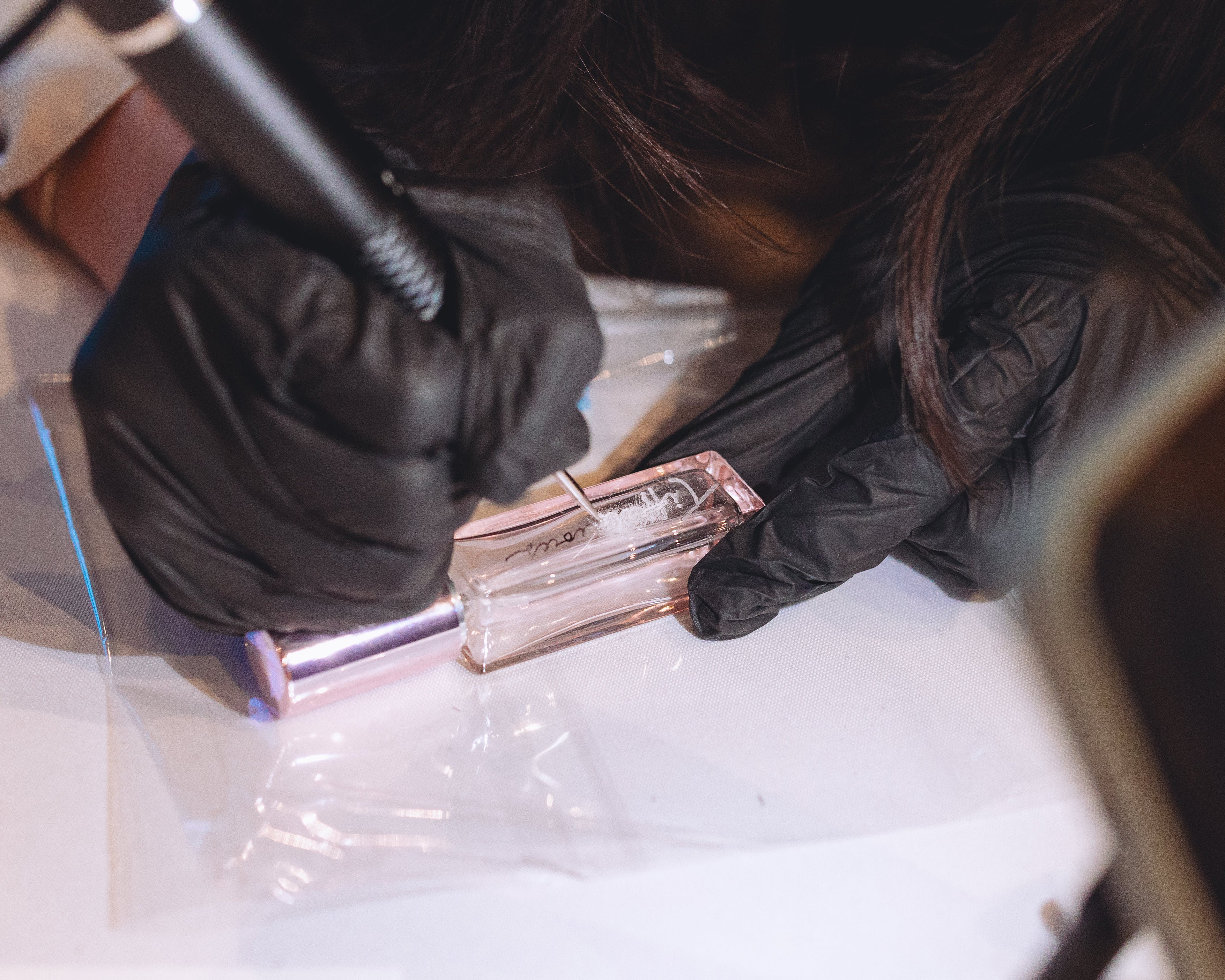 Person wearing black gloves holding a small rectangular object with a reflective surface on a white background.